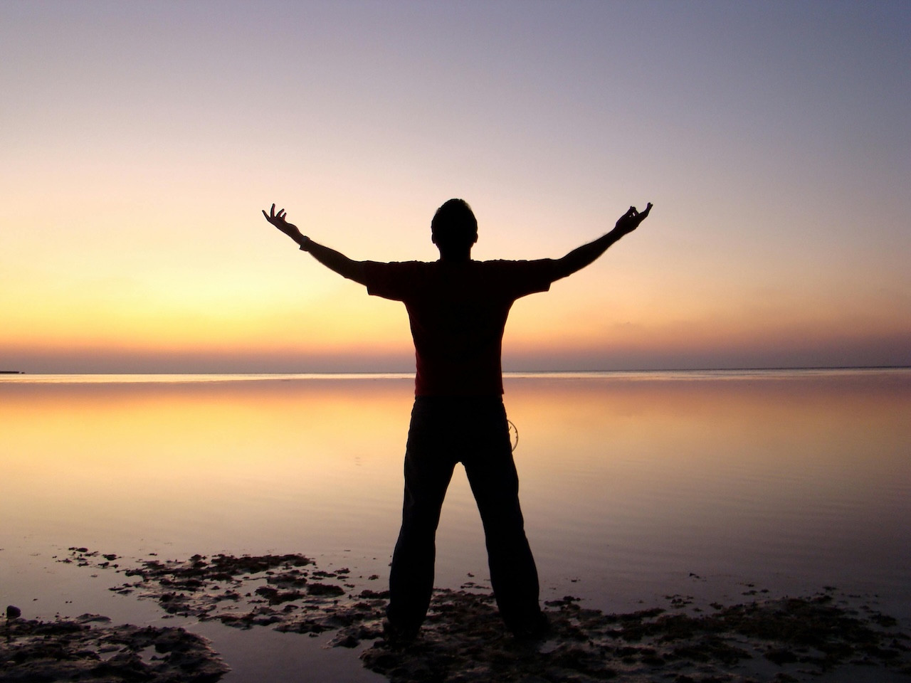 Man with arms raised looking out over the sea