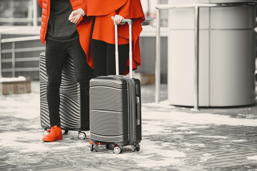 Image of someone wearing a red coat holding a solid suitcase at an airport