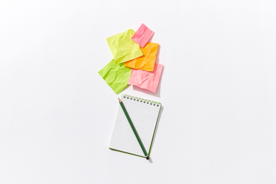 Notepad and coloured post-its on a white background to signify note taking