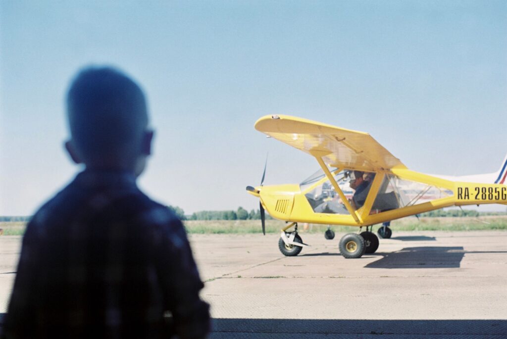 Small child in shadows looking at a yellow plane